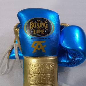 May include: Pair of blue and gold boxing gloves with white laces. The gloves feature the text "NO BOXING NO LIFE" and "HECHO EN MEXICO". The gloves have a gold cuff and accents.