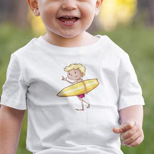 May include: A young child wearing a white t-shirt with a cartoon illustration of a surfer boy. The shirt has a yellow surfboard and the text "Surfer Dude". The child is sitting on a tree stump in a grassy area.