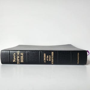 Op de afbeelding: Een zwart lederen gebonden boek met de titel "Nave's Topical Bible: A Digest of the Holy Scriptures" met gouden letters en de naam van de uitgever "Southwestern" op de rug.