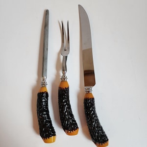 May include: A set of three vintage kitchen utensils with black and orange handles. The set includes a knife, a fork, and a steel.