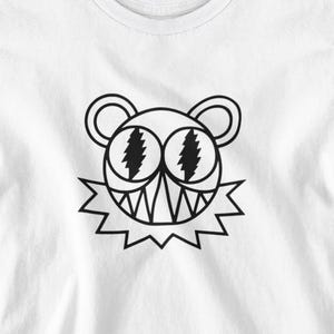 May include: White t-shirt featuring a black cartoon bear face with lightning bolt eyes and a jagged collar. The bear has a wide, toothy grin. The shirt is made of a soft, lightweight material.