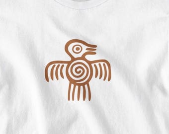 May include: White t-shirt featuring a brown graphic of a bird-like figure with a spiral design on the chest. The design has a minimalist, tribal aesthetic. The shirt is made of a soft, lightweight material.