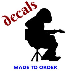 May include: Black silhouette of a person playing a guitar while seated on a stool. The word "decals" is in red script above the figure, and the text "MADE TO ORDER" is in blue block letters below.