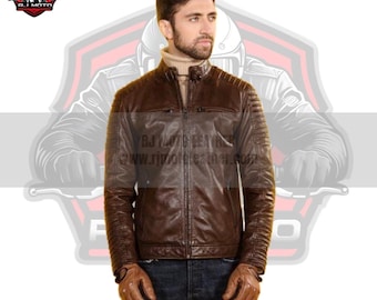 May include: A brown leather motorcycle jacket with a zipper closure and a stand-up collar. The jacket has quilted detailing on the sleeves and a zippered pocket on the left chest. The jacket is worn by a person with a beard and a light brown turtleneck sweater.