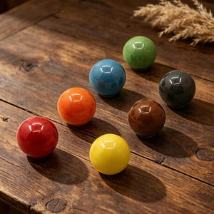 May include: Seven glossy, spherical decorative objects in various colors: red, orange, yellow, blue, green, brown, and dark gray. The spheres are arranged on a wooden surface, reflecting light. The objects appear to be ceramic or glass.