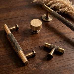 Puede incluir: Una colección de herrajes para armarios de latón y madera, que incluye tiradores y un pomo. Los tiradores presentan un diseño metálico acanalado con detalles de madera. Los herrajes se muestran sobre una superficie de madera oscura.