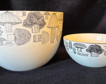 May include: Two white bowls of different sizes featuring a black line-art pattern of various mushroom shapes. The larger bowl is on the left and the smaller bowl is on the right, both decorated with detailed botanical illustrations of fungi.