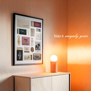 May include: A framed collage of vintage ephemera, including matchbooks, keys, and a small photo, on a light wood wall with a small table lamp. The text "Make it uniquely yours" is visible in the upper right corner of the image.
