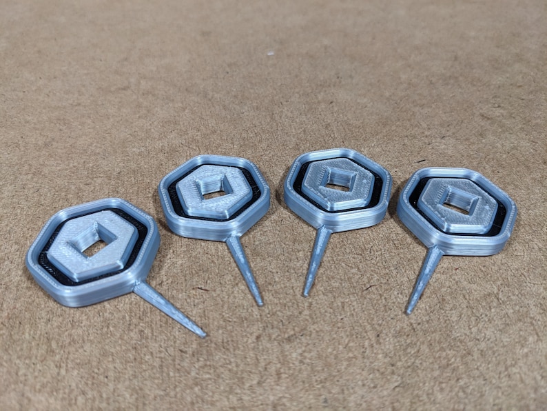 Op de afbeelding: Vier zilverkleurige, 3D-geprinte, zeshoekige gereedschappen met een klein vierkant gat in het midden. Elk gereedschap heeft een puntige punt.