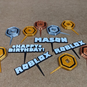 Op de afbeelding: Een set van 10 Roblox-thema caketoppers. De toppers zijn gemaakt van 3D-geprint plastic en hebben verschillende ontwerpen, waaronder het Roblox-logo, de woorden "Happy Birthday!" en "Roblox", en een gouden munt. De toppers zijn perfect om een leuke en feestelijke touch toe te voegen aan elke Roblox-thema verjaardagspartij.