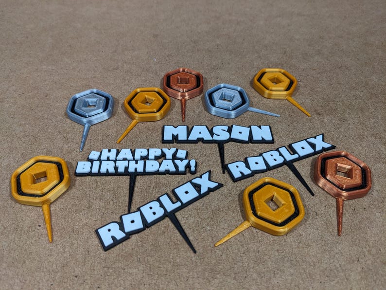 Op de afbeelding: Een set van 10 Roblox-thema caketoppers. De toppers zijn gemaakt van 3D-geprint plastic en hebben verschillende ontwerpen, waaronder het Roblox-logo, de woorden "Happy Birthday!" en "Roblox", en een gouden munt. De toppers zijn perfect om een leuke en feestelijke touch toe te voegen aan elke Roblox-thema verjaardagspartij.