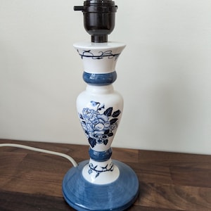 May include: A white and blue ceramic table lamp with a floral design. The lamp features a blue base, a white body with blue floral patterns, and a black lamp holder. The lamp is approximately 12 inches tall.