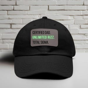 May include: Black baseball cap with a curved brim. A rectangular patch on the front displays the text "CERTIFIED DAD. UNLIMITED RIZZ. TOTAL SIGMA." in white and green lettering. The cap is made of a durable fabric.