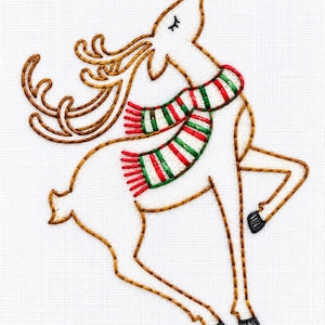 May include: An embroidery design on white fabric featuring a leaping deer outlined in brown thread. The deer has large antlers, black hooves, and wears a scarf with horizontal red, white, and green stripes. The deer's eyes are closed.