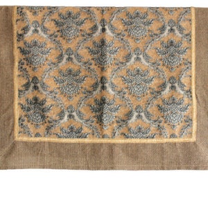 May include: A rectangular decorative textile with a damask pattern in shades of gold, gray, and white. The border is a solid brown with a gold trim. Tassels hang from the bottom corners. This textile is suitable for home decor.