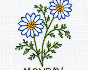 May include: An embroidery design on white fabric featuring two daisies with blue petals and yellow centers, connected by green stems and leaves. Below the flowers, the word MONDAY is stitched in green thread using a simple font.