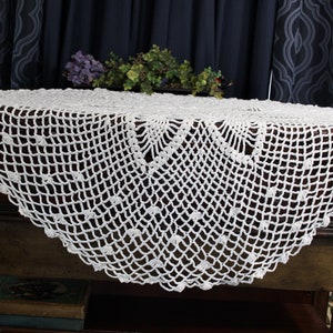May include: White crocheted table runner with a delicate floral pattern. The runner is made of a fine, lightweight yarn and has a scalloped edge.