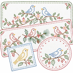 May include: A collection of white fabric pieces featuring cross-stitch embroidery of birds on branches. The set includes two rectangular runners with green and red borders, a square coaster with a blue border, and a round coaster with a red border.