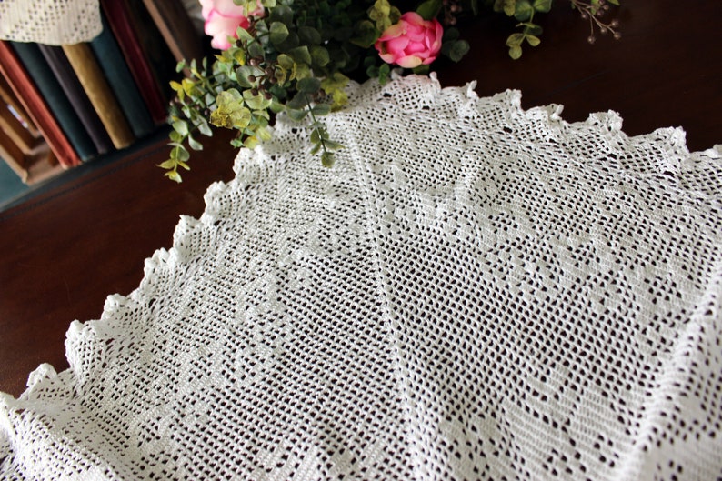 May include: White crocheted doily with a delicate lace pattern. The doily is circular and has a scalloped edge.