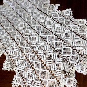 May include: White crocheted table runner with a diamond pattern. The runner has a scalloped edge and is made of delicate lace.