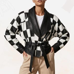 Könnte beinhalten: Schwarz-weiß karierte Lederjacke mit breitem Kragen und Bindegürtel. Die Jacke hat lange Ärmel und wird über einem weißen Hemd und einer beigen Hose getragen. Das Design der Jacke ist ein kühnes, grafisches Statement.