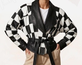 May include: A black and white checkered leather jacket with a wide collar and a tie belt. The jacket has long sleeves and is worn over a white shirt and tan pants. The jacket's design is a bold, graphic statement.