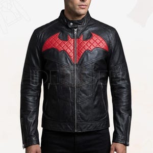 May include: Black leather jacket with a red quilted bat symbol on the chest. The jacket has a stand-up collar, a front zipper, and zippered pockets. The jacket is a classic biker style.