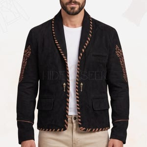May include: A black suede blazer featuring a shawl collar with tan whipstitch detailing, matching tan whipstitch trim along the hem, and intricate tan embroidery on the sleeves. The jacket includes two flap pockets, a chest pocket, and two metal skull-shaped buttons.