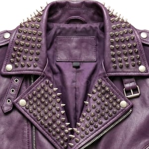 May include: Close-up of a purple leather jacket with silver metal cone studs on the collar and lapels. The jacket has a zipper closure, a small label, and silver button details. The jacket is a classic biker style.