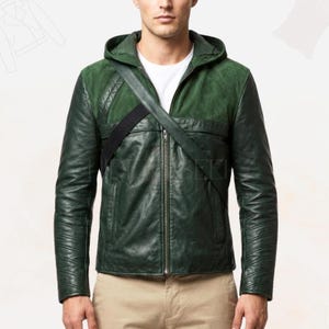 May include: A dark green leather jacket with a hood and a black strap across the chest. The jacket has a zipper closure and a quilted design on the shoulders. The model is wearing a white shirt underneath.
