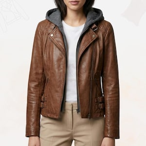 Könnte beinhalten: Braune Lederjacke mit grauem Kapuzeneinsatz. Die Jacke hat einen Reißverschluss, mehrere Taschen und dekorative Schnallen. Die Jacke ist im klassischen Biker-Stil.