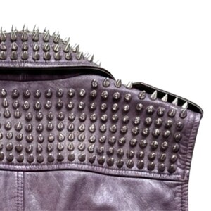 May include: Close-up of a purple leather jacket with numerous silver metal cone studs. The jacket features a notched collar and a studded shoulder detail, showcasing a punk rock aesthetic.
