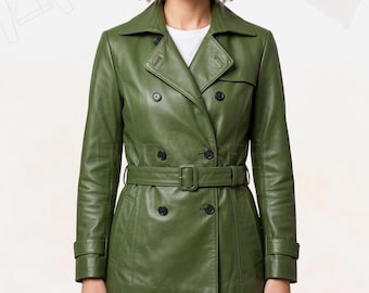 May include: A green leather trench coat with a double-breasted design, a belt, and black buttons. The coat has a classic collar and long sleeves with cuff details. The model is wearing a white t-shirt underneath.