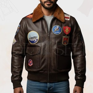 May include: A brown leather bomber jacket with a brown faux fur collar. The jacket features multiple embroidered patches, a front zip, and two front pockets. The jacket has a ribbed hem and cuffs.