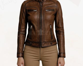 May include: Brown leather jacket with a stand-up collar, zipper closure, and multiple zippered pockets. The jacket has a fitted silhouette and is worn with tan pants. The jacket's design includes stitching details and a classic biker style.