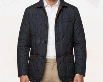 May include: Navy blue quilted jacket with brown corduroy collar and pocket trim. The jacket has a button-up front and two front pockets. The model is wearing a white dress shirt and khaki pants. A classic outerwear piece.