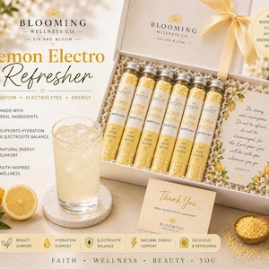 May include: A white gift box containing six glass tubes of yellow Lemon Electro Refresher powder, a glass of yellow liquid, a thank you card, and a card with Joshua 1:9 text. The box features a yellow ribbon and branding for Blooming Wellness Co.