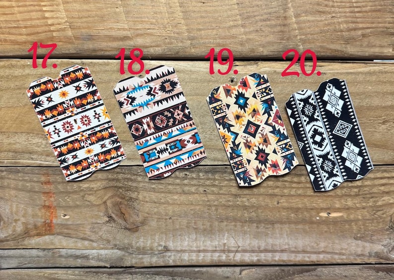 Puede incluir: Cuatro llaveros decorativos con patrones del suroeste. Los llaveros presentan dise&ntilde;os geom&eacute;tricos en varios colores, incluyendo naranja, blanco, negro y turquesa, sobre un fondo de madera.