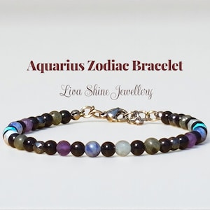 May include: Aquarius Zodiac Bracelet. A beaded bracelet with a variety of colorful gemstones, including purple, blue, and black beads. The bracelet has a gold-colored chain and clasp. The text "Aquarius Zodiac Bracelet" and "Liva Shine Jewellery" are displayed above the bracelet.