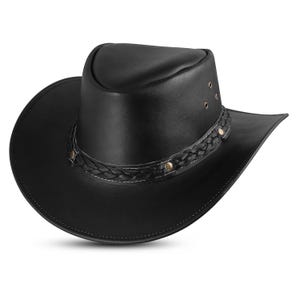 Op de afbeelding: Een zwarte leren cowboyhoed met een gevlochten band en gouden accenten.