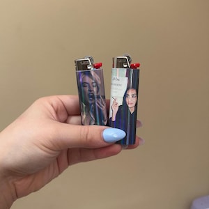 May include: Two lighters with images of women. One lighter has a woman with her mouth open, and the other has a woman holding a cigarette. Both lighters have a red ignition button.