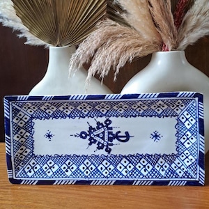 May include: A rectangular ceramic serving tray with a blue and white geometric pattern. The tray has a white background with a blue border and a central design featuring a stylized geometric motif.