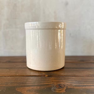 May include: A white ceramic mug with a black handle and the text "But First, Coffee" in a black, handwritten-style font. The mug is on a white surface.