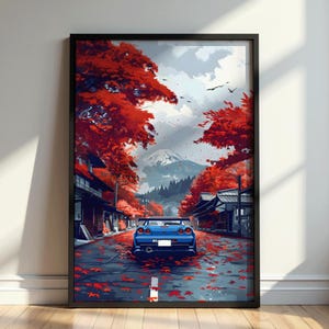 May include: A framed wall art print depicting a blue sports car parked on a street covered in fallen red maple leaves. The scene features traditional buildings on both sides, vibrant red trees, and a snow-capped mountain in the distance.