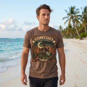 Peut inclure: Un t-shirt marron à manches courtes avec une impression graphique représentant une maison hantée, un croissant de lune, des chauves-souris et des citrouilles. Le texte indique HALLOWEEN RETRO VINTAGE EST. 1892, entouré de branches et feuillages.