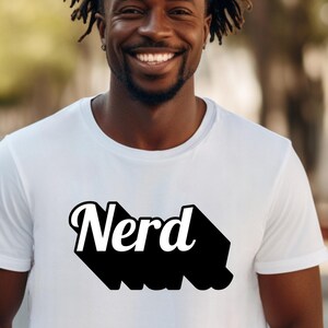 Può includere: Una maglietta bianca con una grafica nera in stile retrò che dice "Nerd" in lettere bianche.