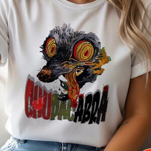 May include: White t-shirt featuring a graphic of a creature with large, red and yellow eyes, a gray snout, and a long, red tongue. The word "CHUPACABRA" is printed in a stylized font below the creature.