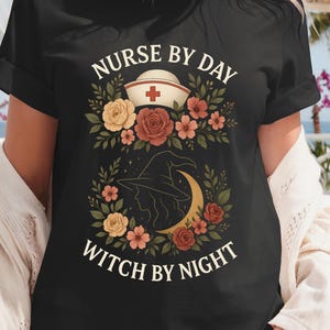 Può includere: T-shirt nera con la scritta "NURSE BY DAY WITCH BY NIGHT". Il design include un cappello da infermiera e un cappello da strega con una luna crescente, circondati da elementi floreali gialli, rossi e rosa.