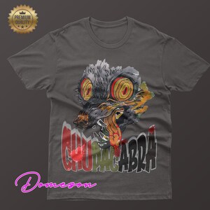 May include: Dark gray t-shirt featuring a watercolor illustration of a Chupacabra with large yellow eyes and sharp teeth. The word "CHUPACABRA" is printed in a distressed font below the creature.
