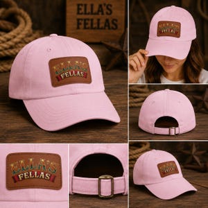 Può includere: Un cappellino da baseball rosa chiaro con una toppa rettangolare in pelle marrone sul davanti. La toppa riporta la scritta ELLA'S FELLAS in un carattere stilizzato. Il cappellino presenta una visiera curva, occhielli cuciti e un cinturino.